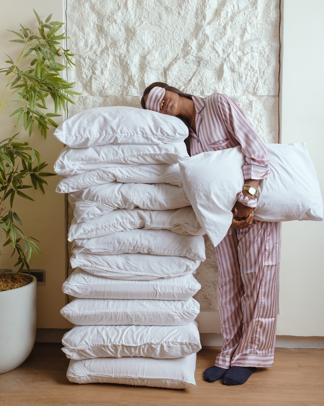 Woman in a blush striped set resting against a tall stack of white pillows