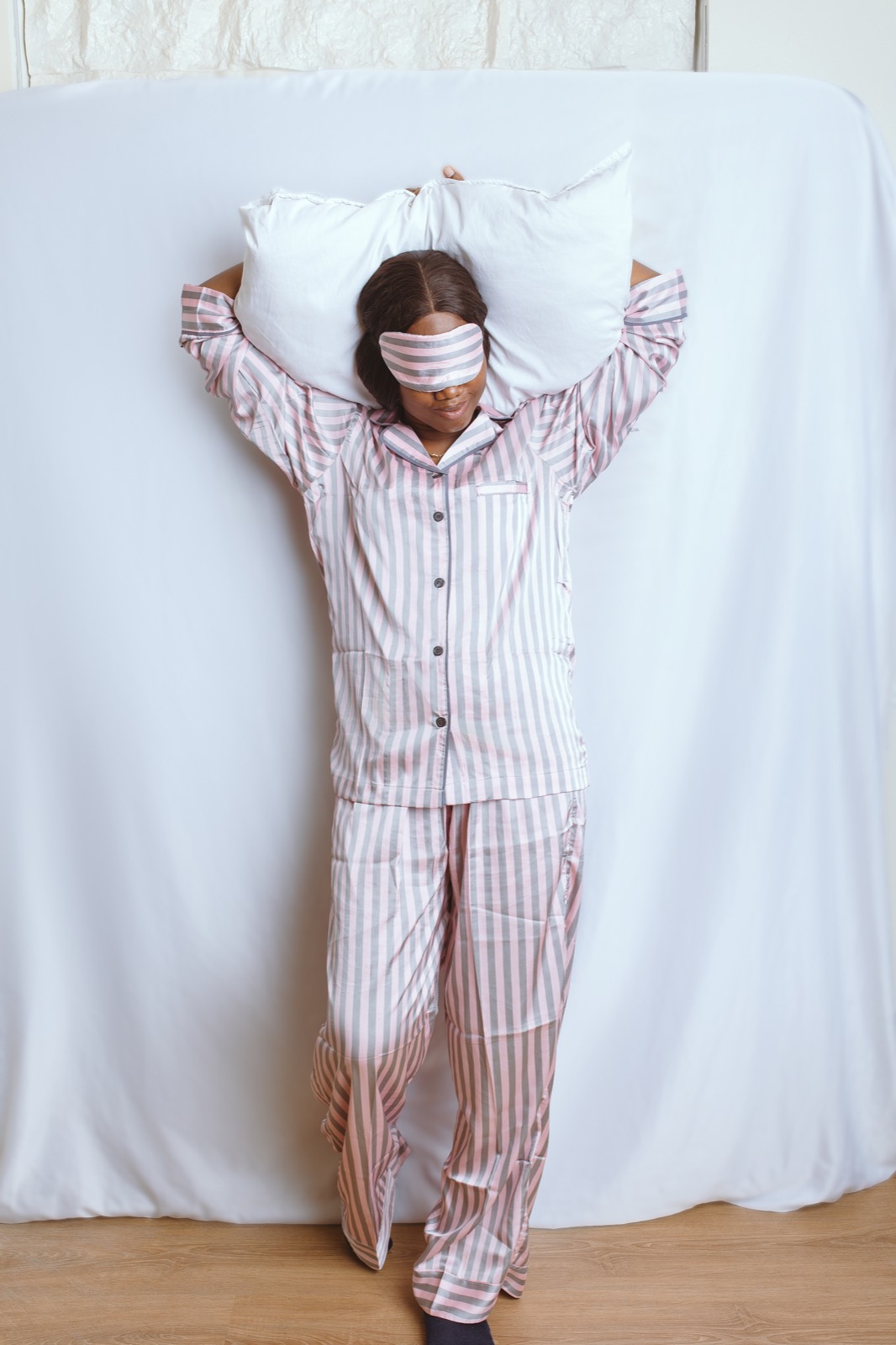Woman in a blush grey striped set holding a pillow overhead